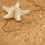 Schlichte Basic-Kette mit minimalistischem Design, liegend auf feinem Sand und Seesteinen am Strand. Die zeitlose Kette fügt sich harmonisch in die natürliche Umgebung ein und symbolisiert schlichte Eleganz.